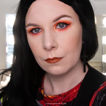 A close up shot of a woman with a black wig and orange eyeshadow and lipstick.