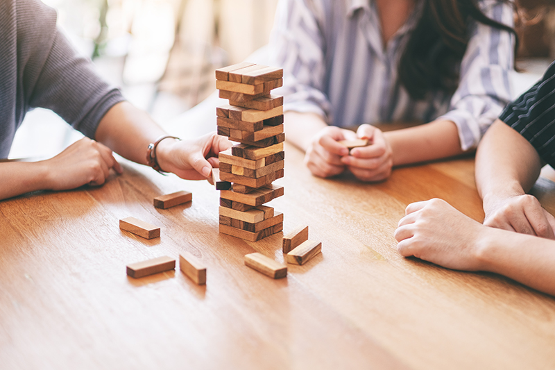 Closeup image of three friends sitting and playing Tumble tower wooden block game together By Farknot Architect on adobe stock