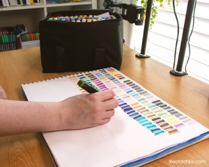 A Hand swatching alcohol markers on a peice of white paper.