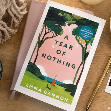 a photo of the books cover with various decorative items around it, a cup of tea, a journal and pen, photos, flowers and crystals