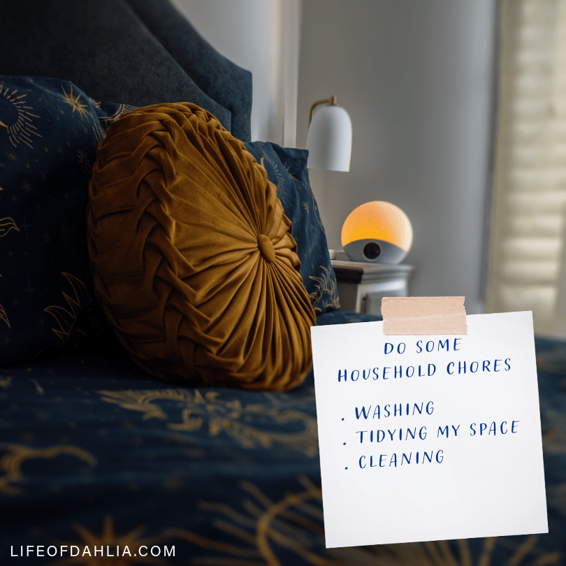 A photo that feature a dark bedroom with a cozy looking bed, featuring a blue and gold colour scheme and a lamp in the background. And a piece of paper in the foreground that has a list of house hold chores written on it.