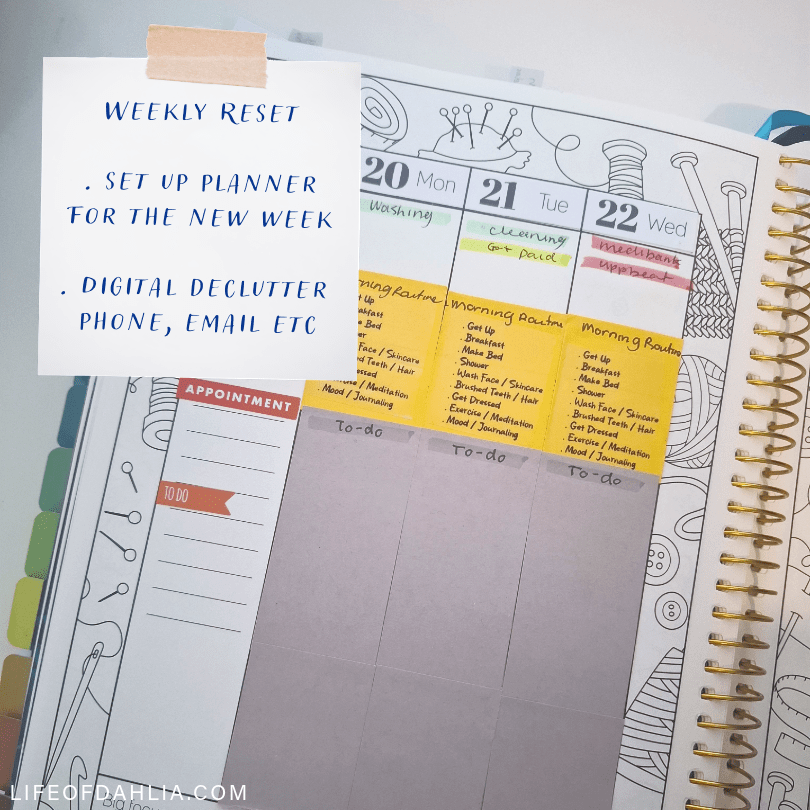 A photo that feature a colouring planner by Sarah Renae Clarke. And a piece of paper in the foreground that talks about doing a weekly reset.